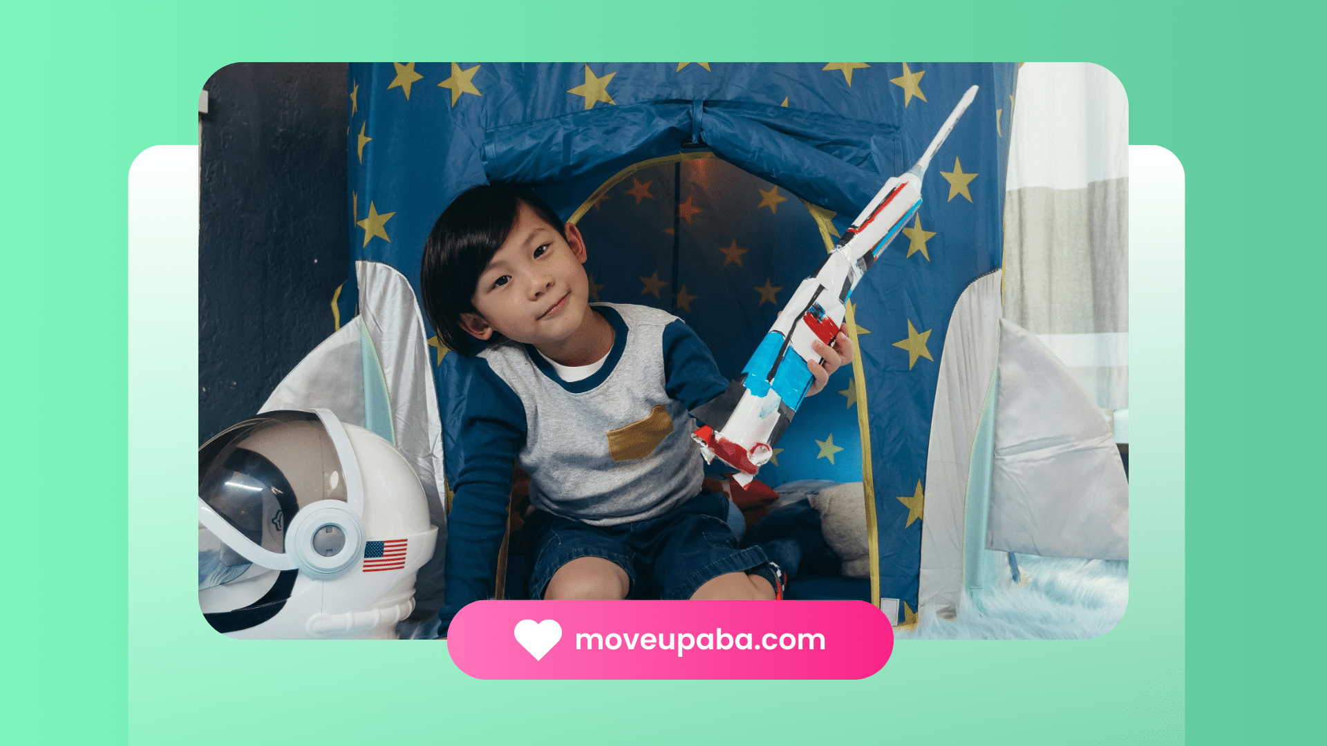 A young boy sitting in a play tent decorated with stars, holding a toy rocket and next to an astronaut helmet, during an ABA therapy session