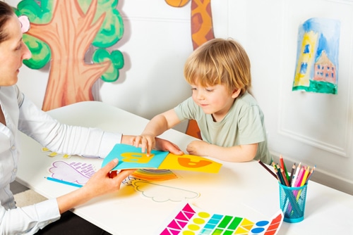 Early development lesson, woman shows and teaches letters to little blond boy pointing to the page in the book