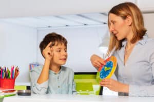 A therapist guides a child through an ABA therapy session using a clock to teach time and improve cognitive skills.