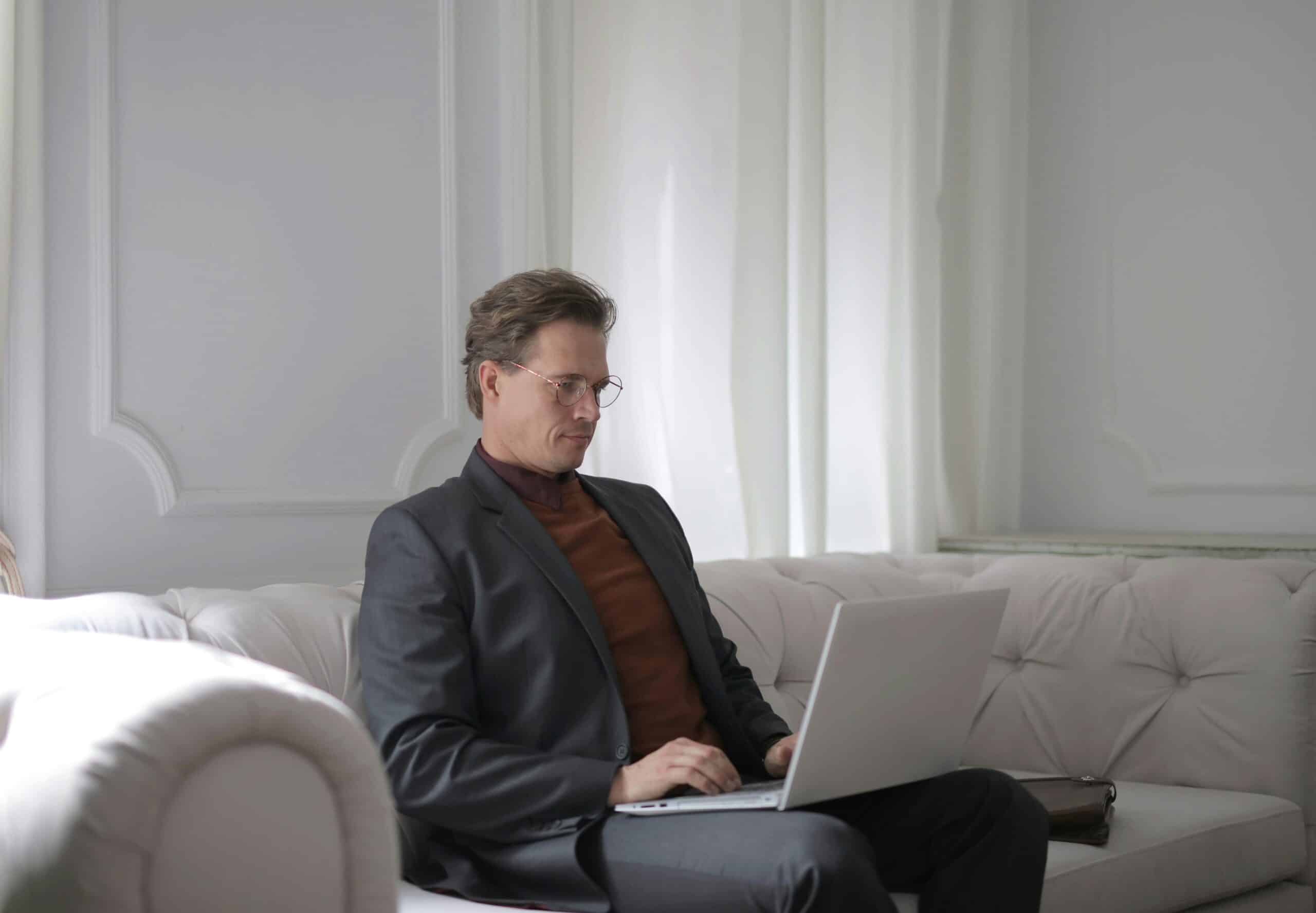 BCBA man typing on his laptop, sitting on the white sofa