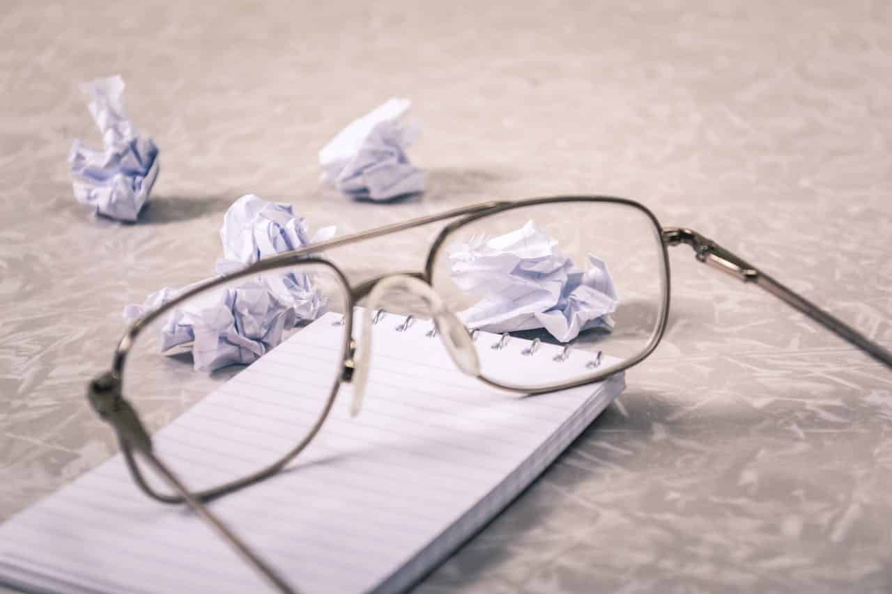 Glasses on top of a notebook with crumpled paper in the back