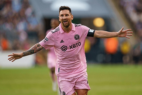 Lionel Messi in a pink jersey celebrating with arms wide open, likely after scoring a goal