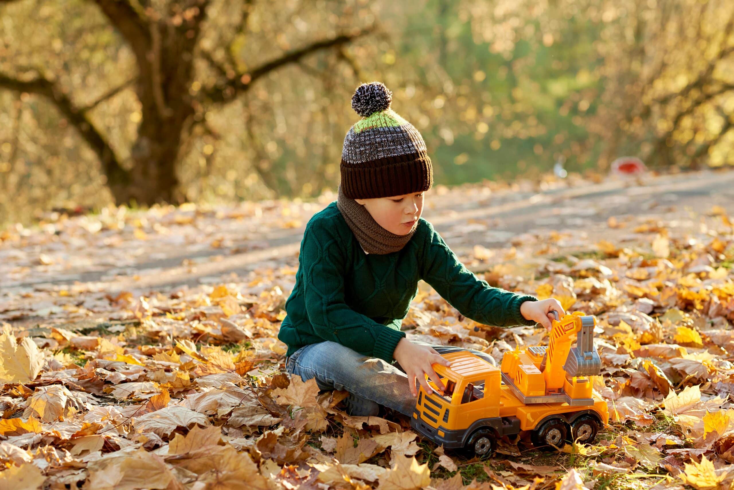 boy playing with a toy truck on the ground in autumn