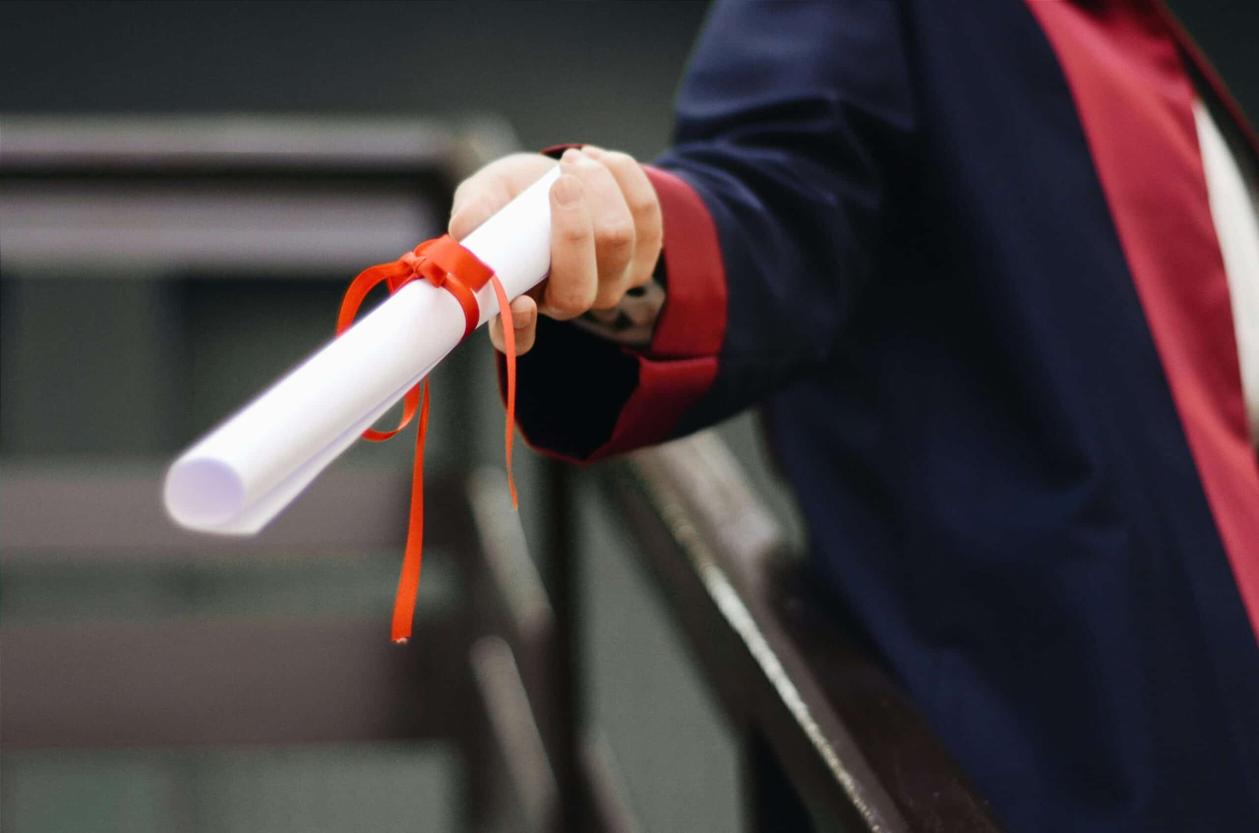 certification rolled up with a ribbon held by a graduate