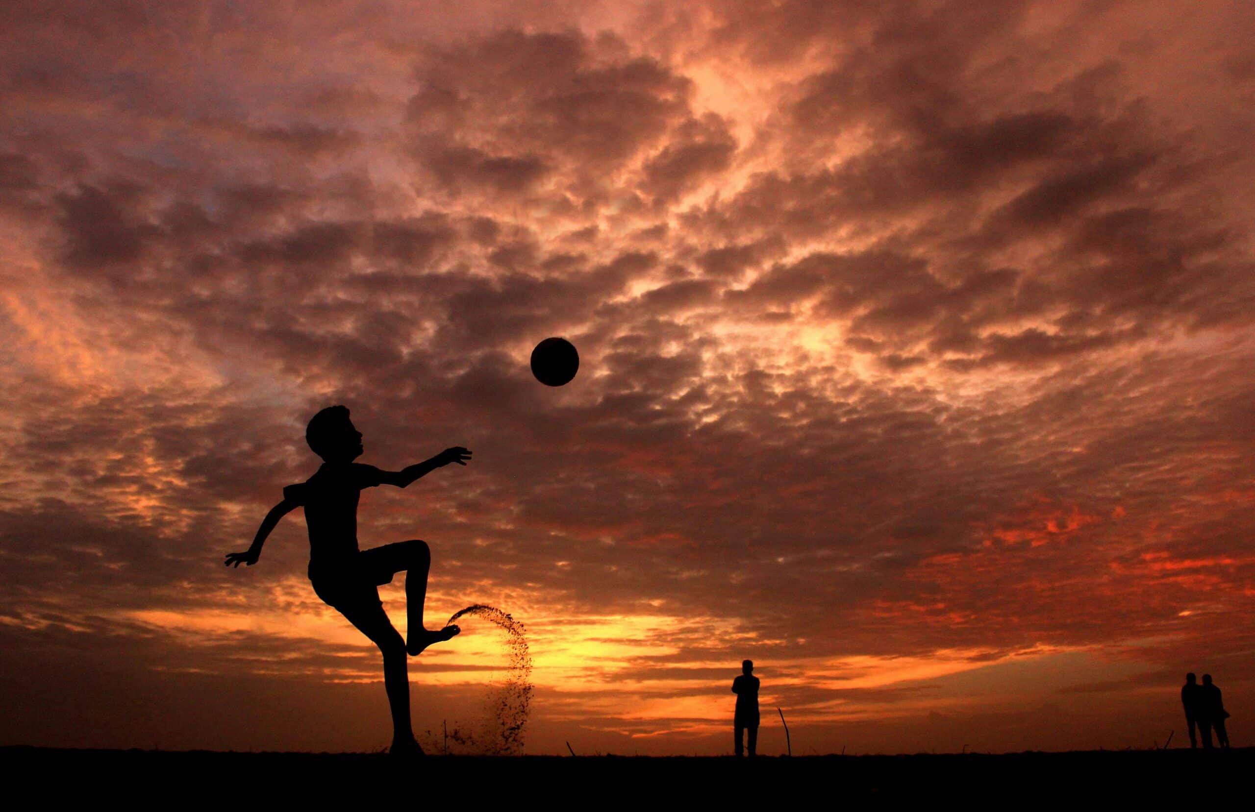 silhouette of a kid playing soccer with his father nearby