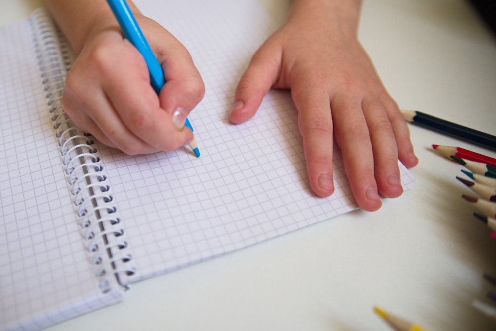 Someone writing in a checkered notebook, symbolizing practice of Behavior Analysis Techniques.