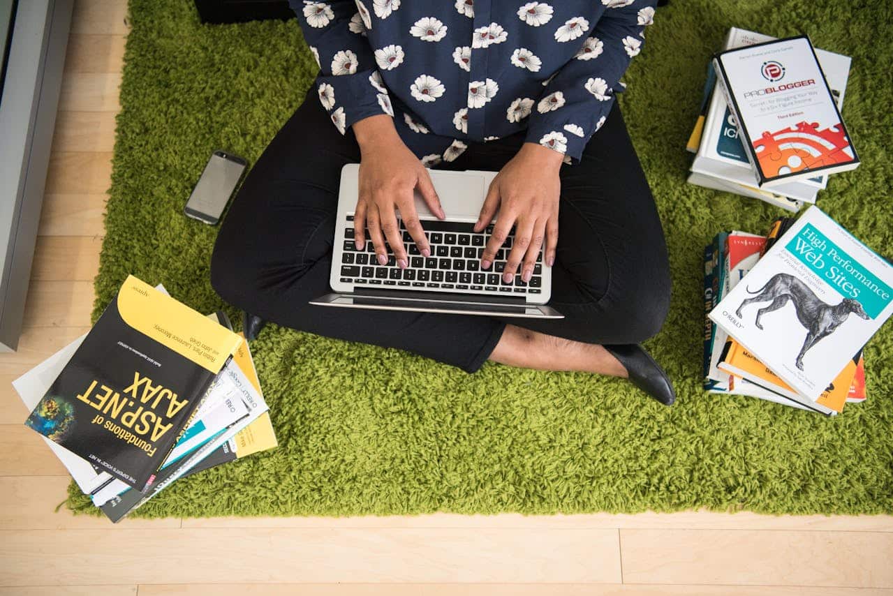 Person typing in a laptop with books aound him