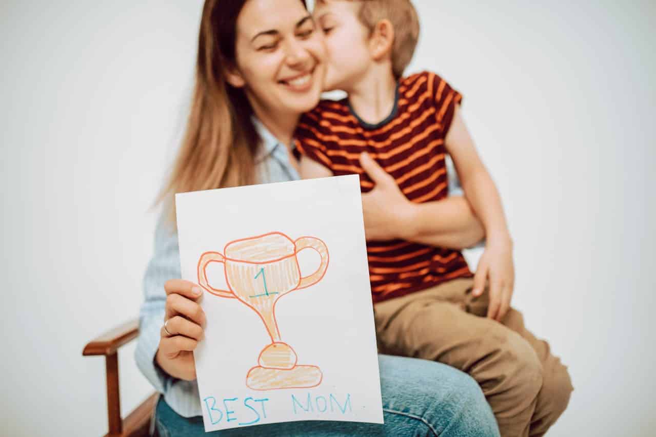 child on mom's lap with a trophy written on paper