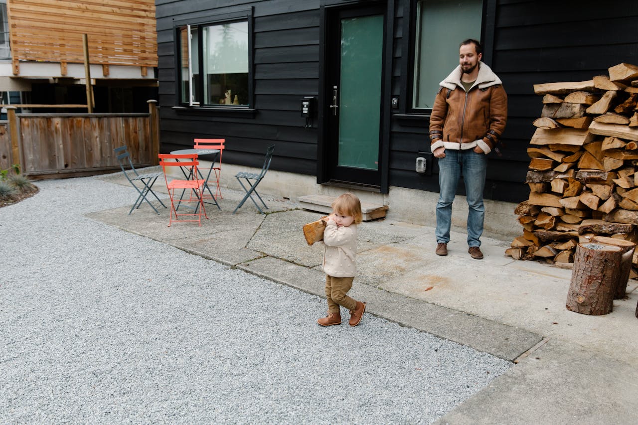 dad watching his son carry a small log in the front yard