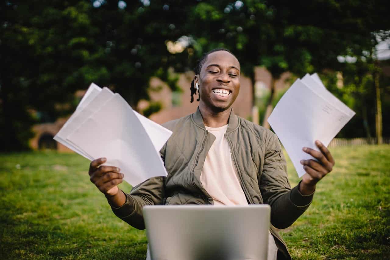 happy guy holding paperworks with a laptop on his lap