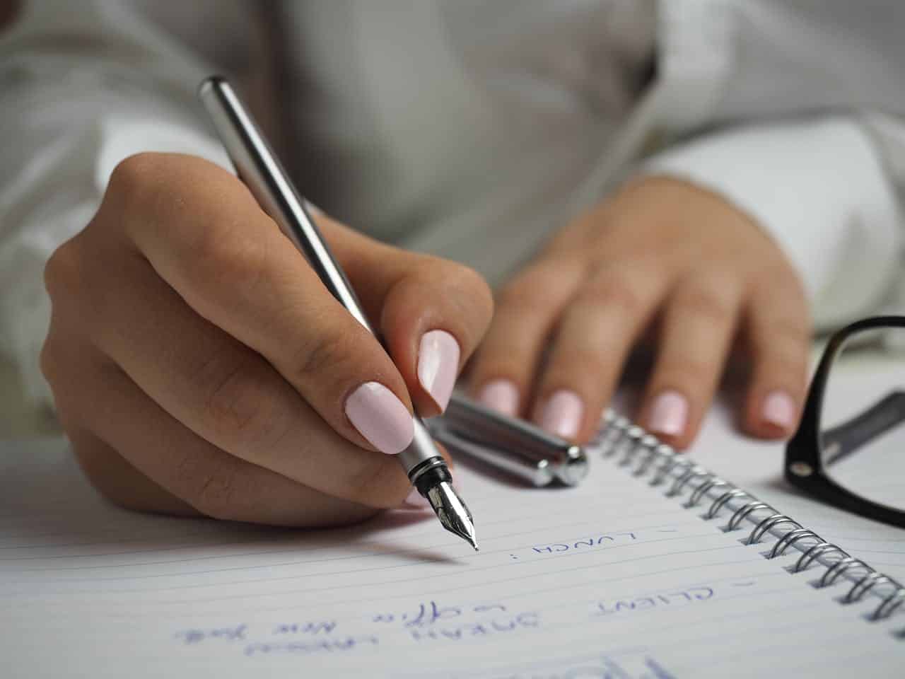 person writing on a notebook with a silver pen