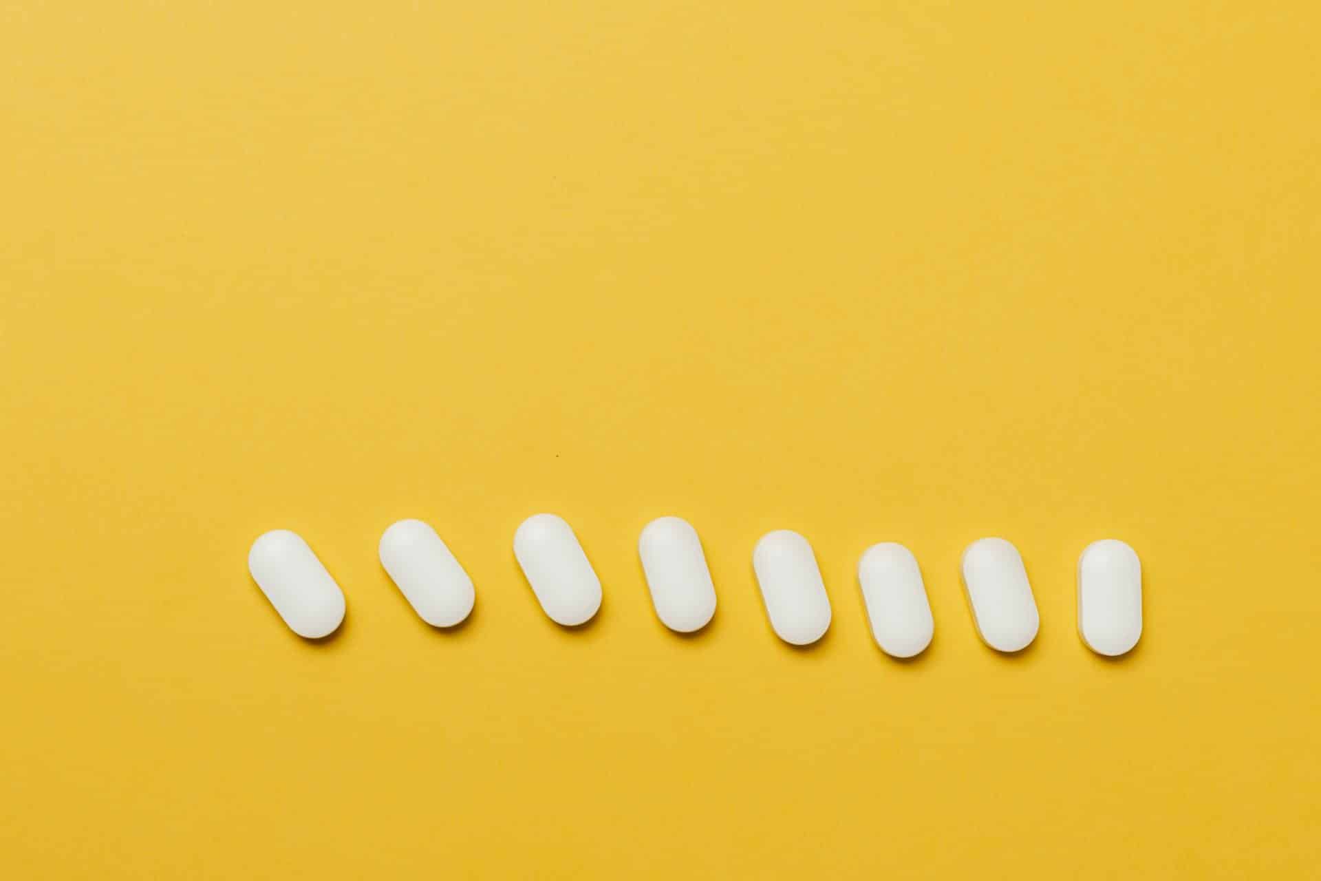 white pills laid out in a line on a yellow backdrop