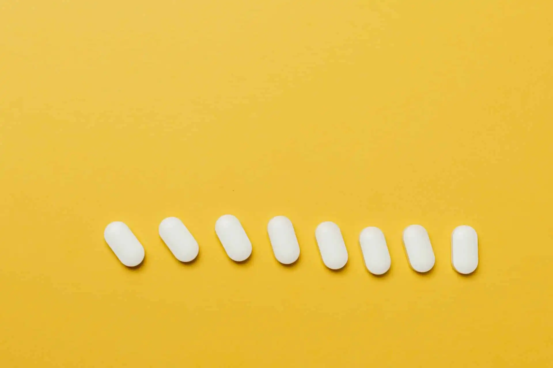 white pills laid out in a line on a yellow backdrop