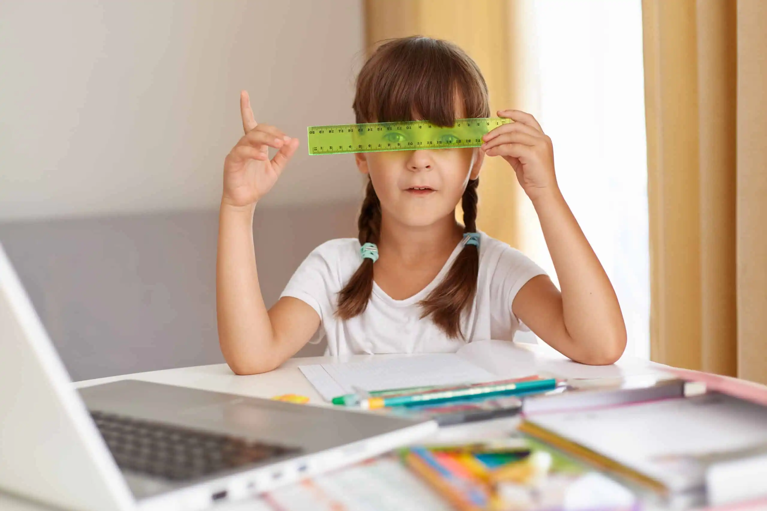 A girl with autism study on a table holding a green ruler in front of her face
