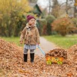 A child with autism playing joyfully with autumn leaves alone in an outdoor park in Maryland.