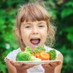 Young girl holding a plate of vegetables.