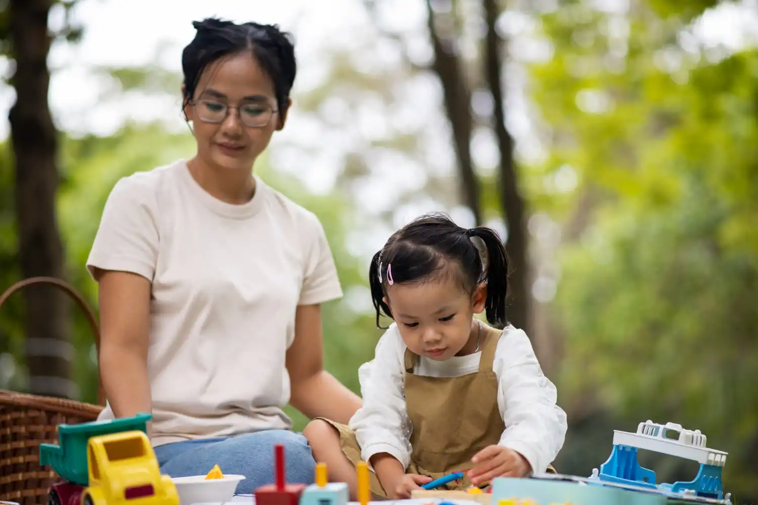 ABA therapist and little girl playing with toys in the park.