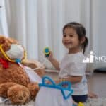 A little child playing doctors with dolls at home.