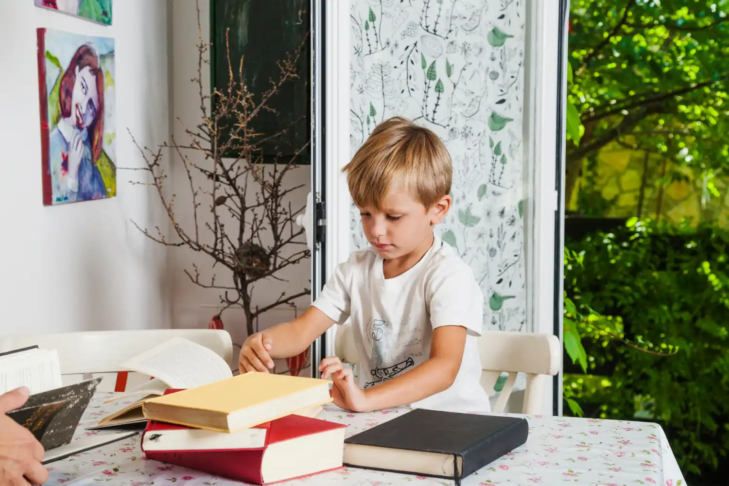 Young boy sitting at a table with a stack of books.