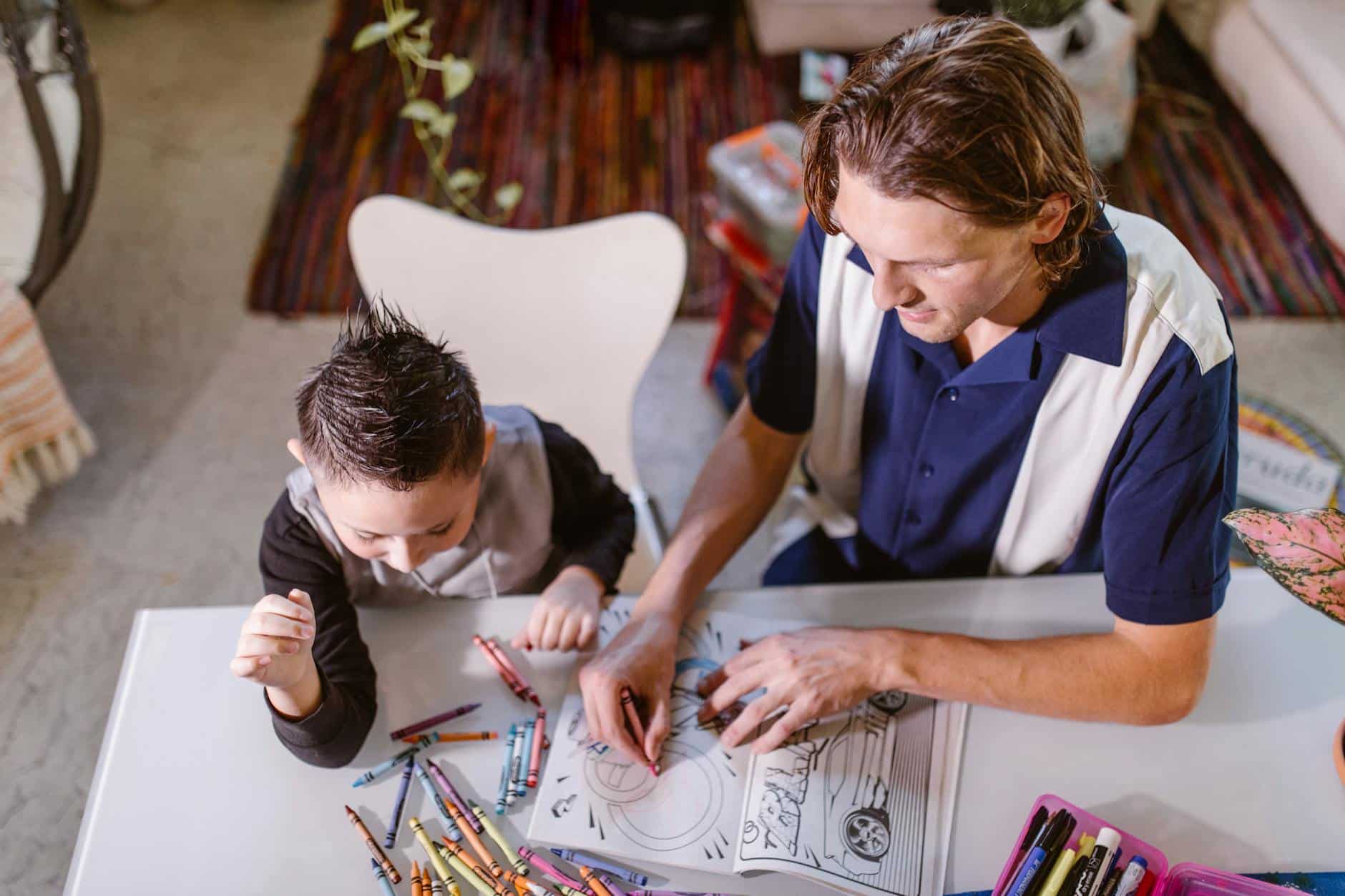 BCBA helping an autistic child color in a coloring book with crayons scattered on the table in MD.