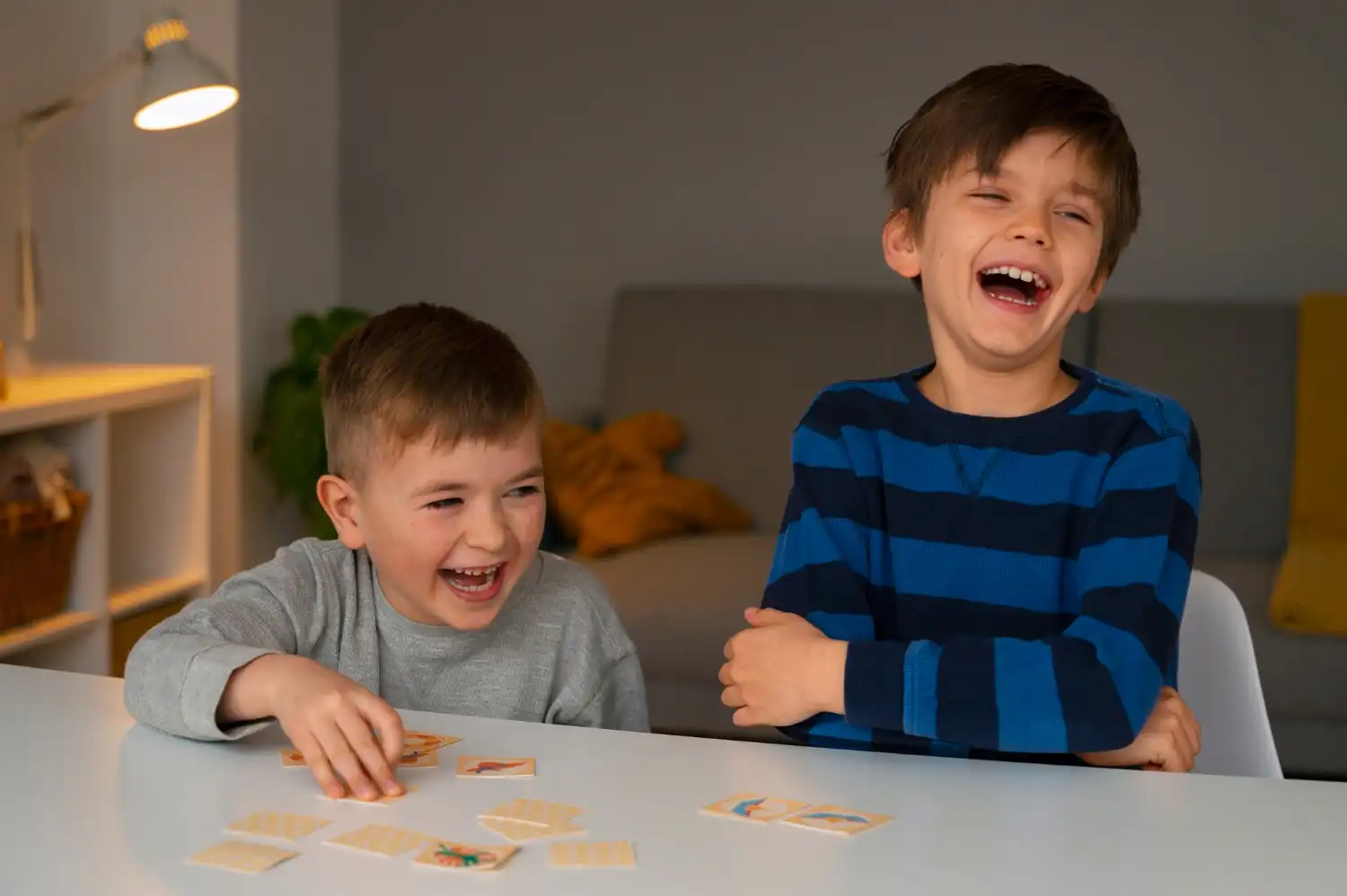 Two young boys laughing while playing a memory card game.