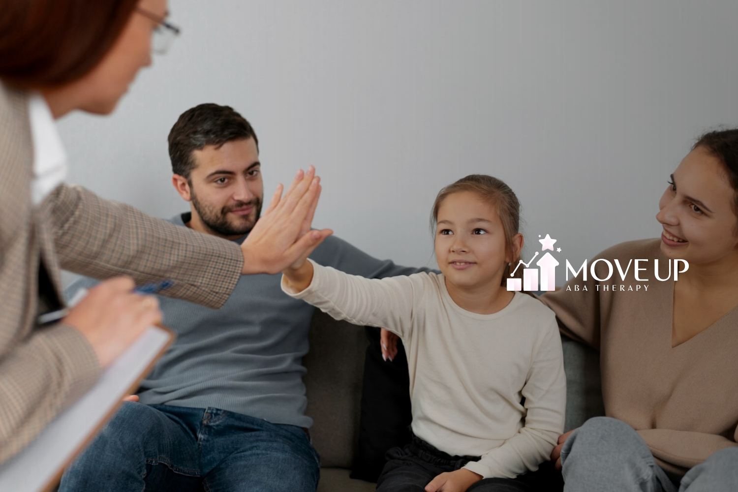 Young girl giving a high-five to ABA therapist while sitting on a couch with her smiling parents.