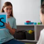 Speech therapist holding a flashcard with the letter "S" while teaching a young child.