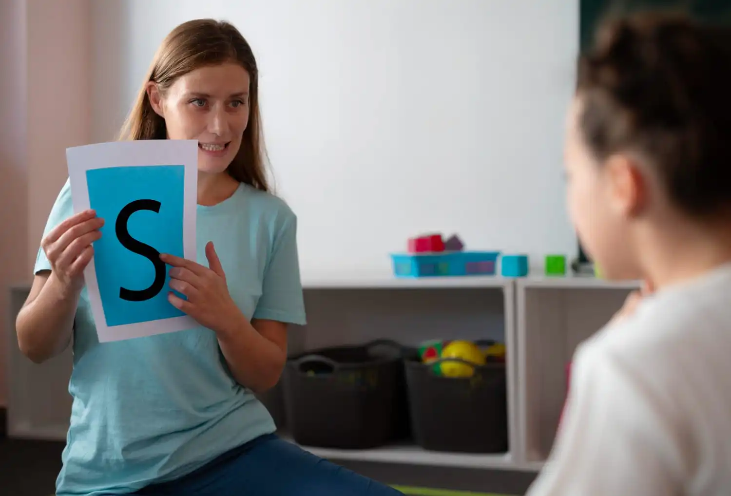 Speech therapist holding a flashcard with the letter "S" while teaching a young child.