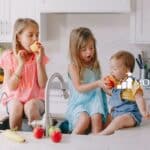 Three little kids eating fruits in the kitchen