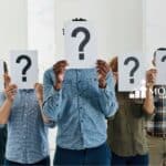 A group of people holding a paper with huge "question mark" on it.