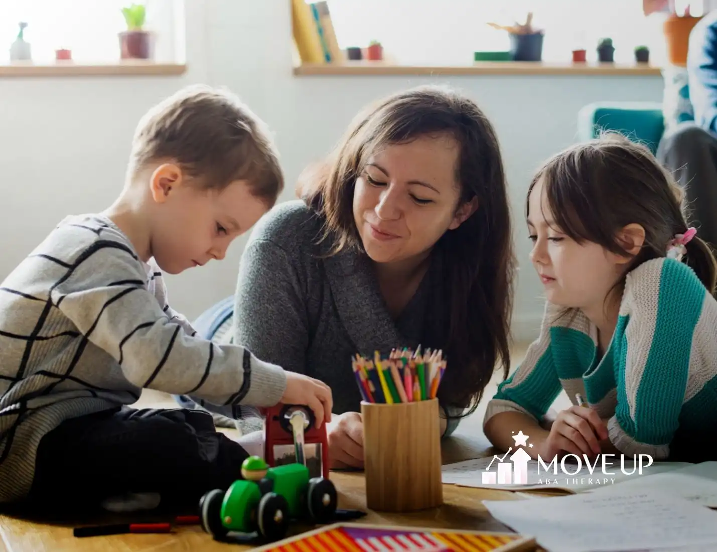 Two children and a BCBA sitting on the floor, playing with toys.