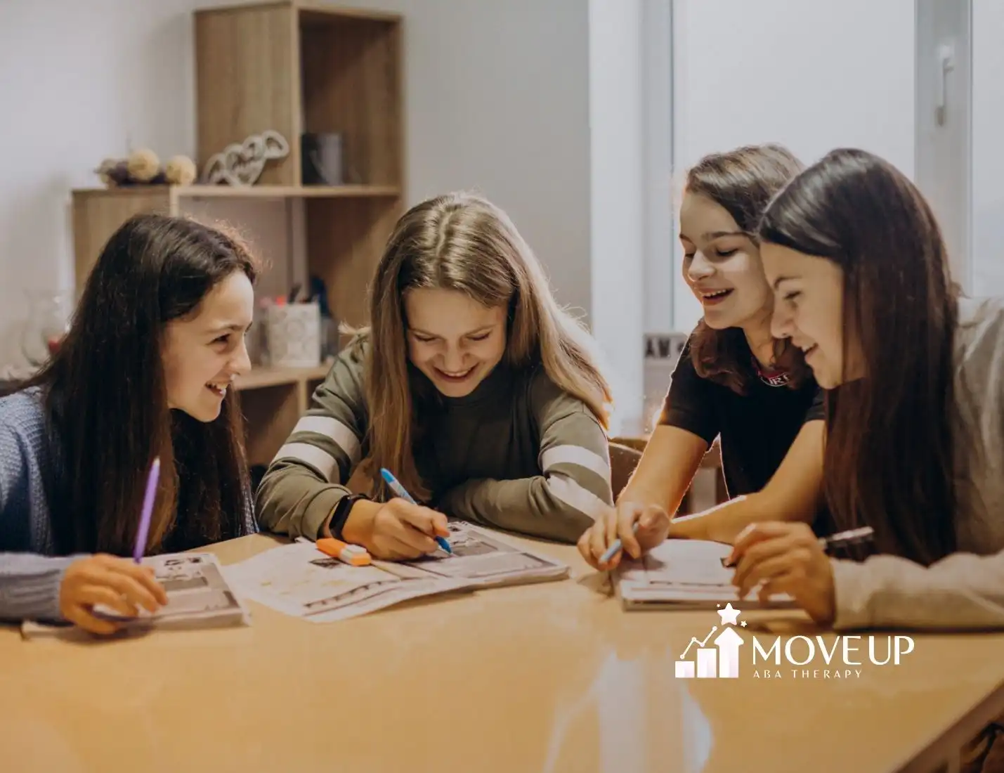 Four teenage girls sitting around a table, drawing and laughing together.