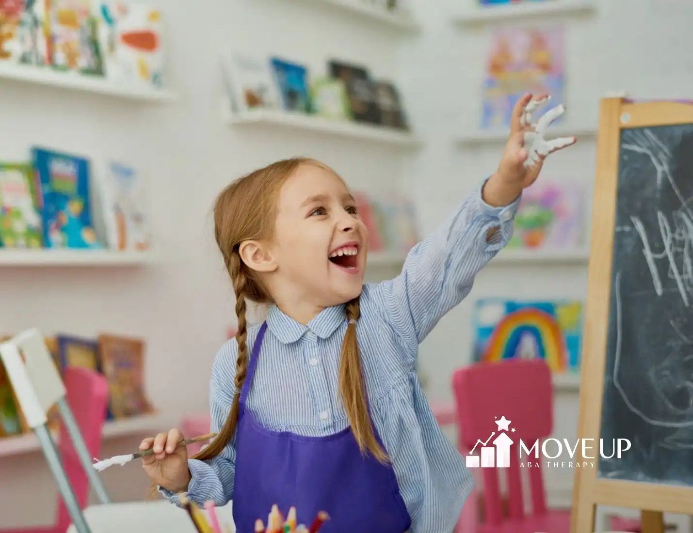 Autistic girl with pigtails smiling and painting at a chalkboard.