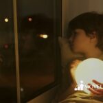 An autistic child holding a glowing orb while staring out the window at night in Maryland.