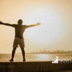 An autistic man standing with arms outstretched toward the sunrise by the ocean in Virginia.