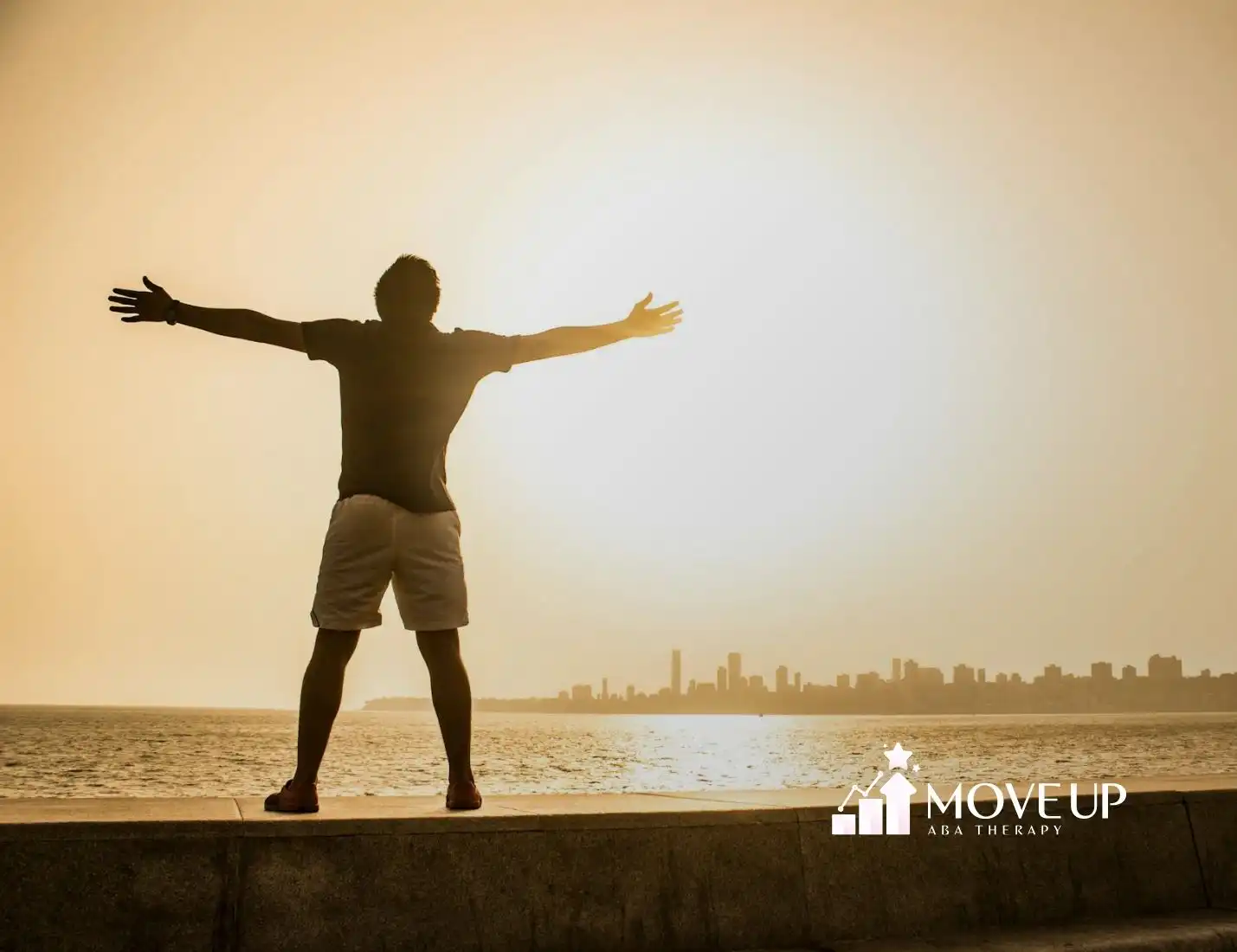 An autistic man standing with arms outstretched toward the sunrise by the ocean in Virginia.