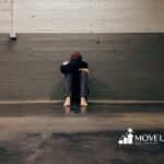 An autistic person sitting on the floor with head on knees against a gray wall in Virginia.