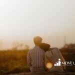 An autistic couple sitting outdoors at sunset, with the woman resting her head on the man’s shoulder in MD.