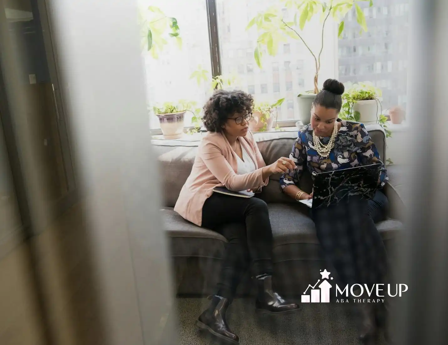 A BCBA supervising an RBT student with her ABA session plan on laptop in bright office space in MD.