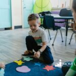 An autistic boy playing with colorful paper cutouts on the classroom floor during ABA therapy in MD.