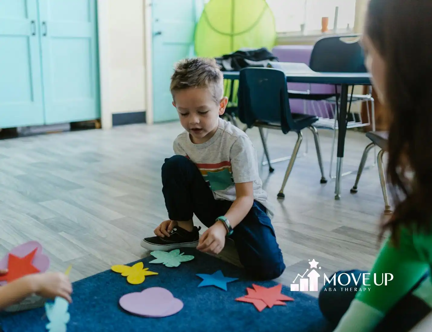 An autistic boy playing with colorful paper cutouts on the classroom floor during ABA therapy in MD.