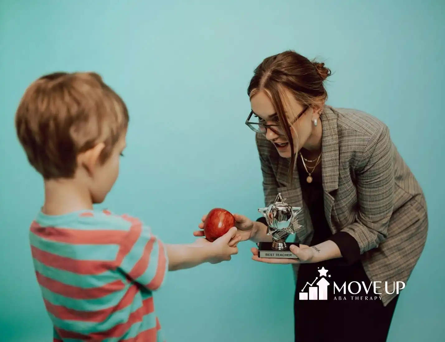 Autistic child receives apple and trophy to a smiling ABA therapist during ABA therapy in Maryland.