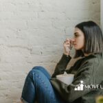 A BCBA sitting by a wall holding tissues and a cup, looking emotional during ABA therapy session in Virginia.