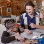 An ABA therapist helping an autistic boy with SPD color in a book at a table with crayons at home in Virginia.