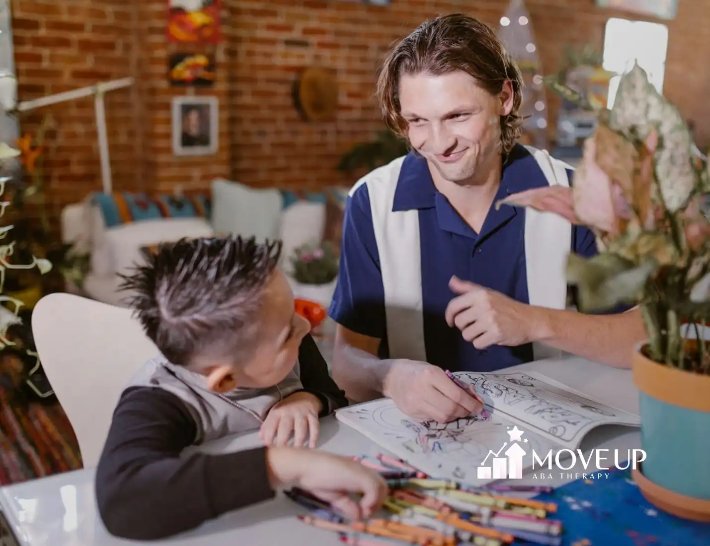 An ABA therapist helping an autistic boy with SPD color in a book at a table with crayons at home in Virginia.