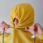 Person pulling the strings of a yellow hoodie tight, covering their face except for the eyes and nose