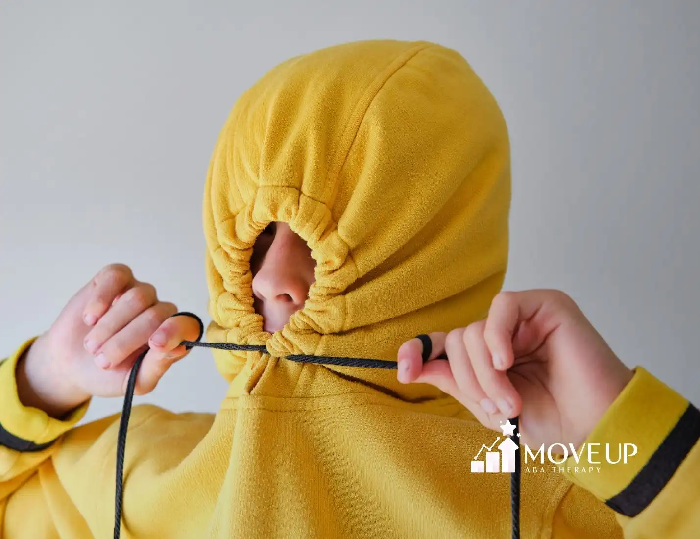 Person pulling the strings of a yellow hoodie tight, covering their face except for the eyes and nose