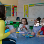 Teacher or therapist engaging with three young children at a table, illustrating an interactive approach potentially used in Pivotal Response Training (PRT) for autism.