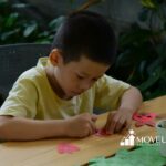 An autistic boy in yellow shirt focusing on a craft activity with paper cutouts during in-home ABA therapy in Virginia.