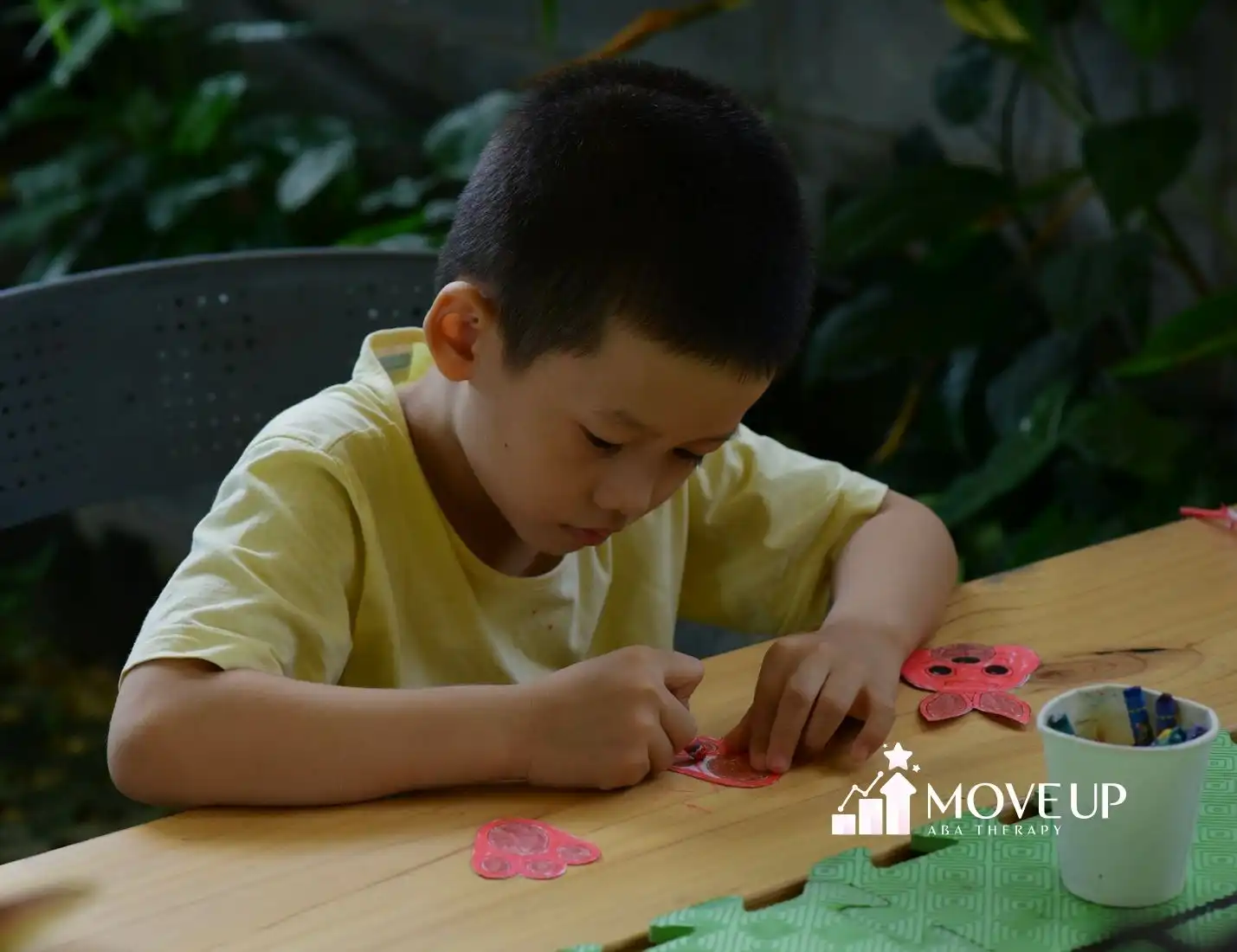 An autistic boy in yellow shirt focusing on a craft activity with paper cutouts during in-home ABA therapy in Virginia.